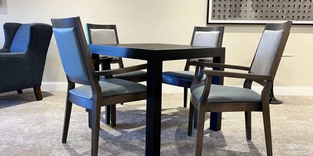 A dining table with four bariatric chairs and a bariatric chair. High weight capacity, padding, adjustable components, armrests for patient comfort and safety.